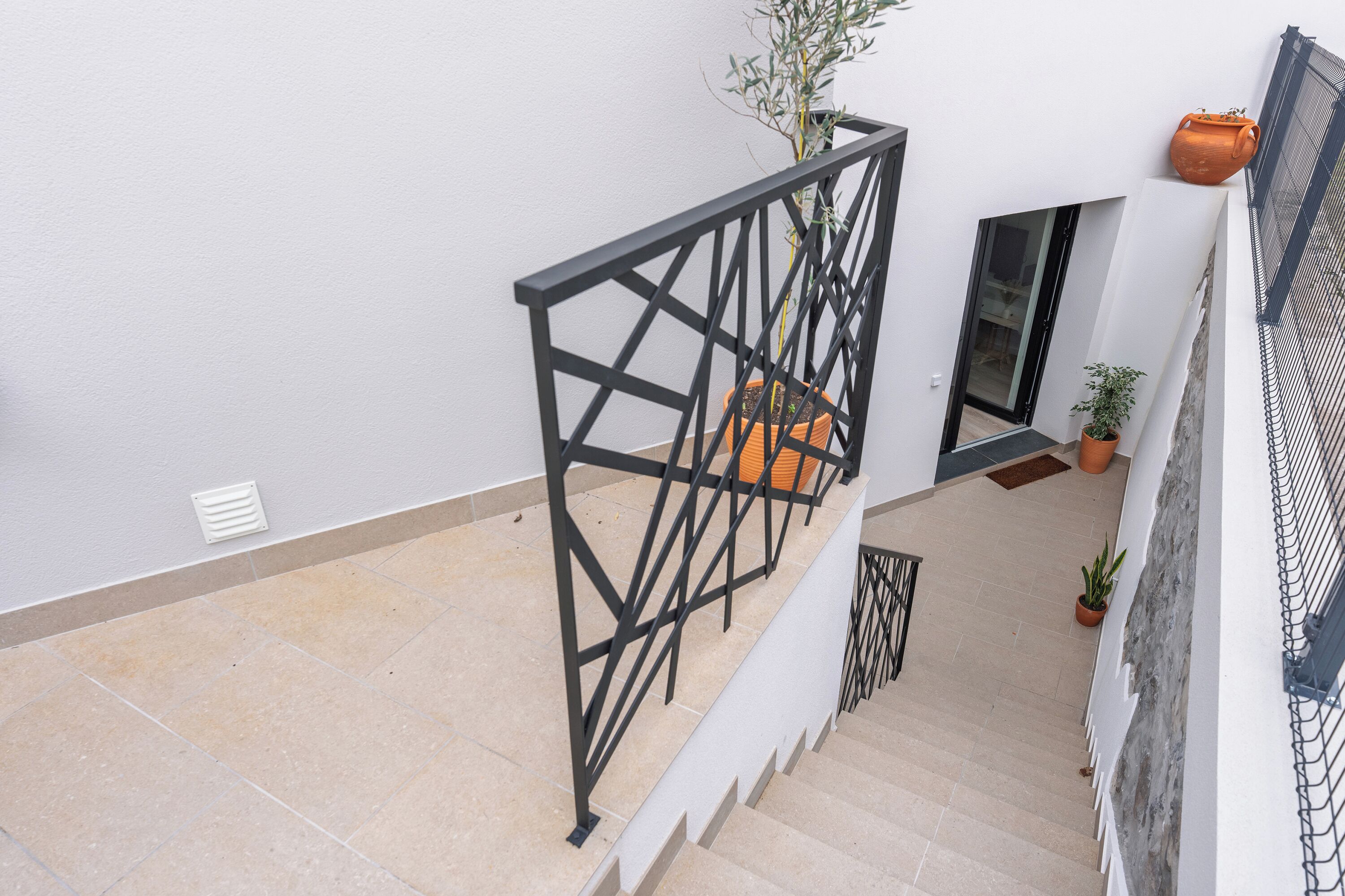 Un escalier avec une rampe en métal noir, des plantes en pot et un mur blanc.