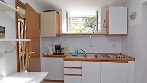 A compact kitchen with white cabinets, a wooden countertop, a sink, and a window with a view of greenery. - Studio Veli  A in Veli Lošinj (Veli Lošinj)
