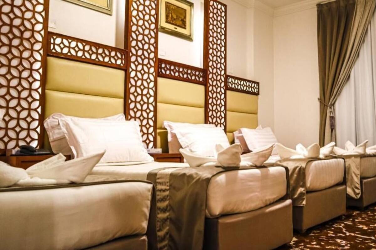 A hotel room with two beds, a wooden headboard, a patterned wall, and a large window with curtains.