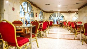 A dining area with red upholstered chairs and gold frames, arranged around round tables. - Mukhtara Al Gharbi Hotel (Madinah)
