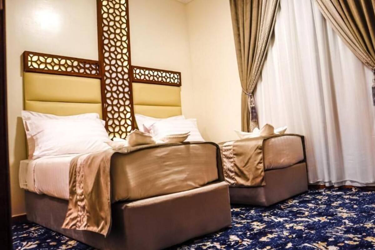 A hotel room with two beds, a patterned carpet, and a decorative headboard.