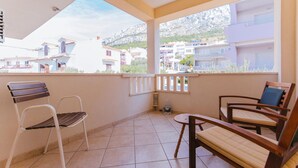 A balcony with two wooden chairs and a small table, overlooking a residential area with buildings and a mountain in the background. - 1 bedroom beautiful apartment in Omis (Omis)