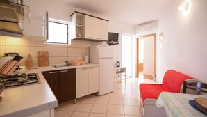 A compact kitchen with a gas stove, a sink, and cabinets. There is a small dining area with a red chair and a table. - 1 bedroom beautiful apartment in Omis (Omis)
