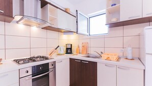 A modern kitchen with white cabinets, a gas stove, an oven, a coffee maker, and a window above the sink. - 1 bedroom beautiful apartment in Omis (Omis)