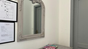Une pièce avec un grand miroir décoratif, une liste de prix encadrée et une petite table sur laquelle se trouve un sac.