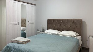 Une chambre à coucher avec un lit, une table de chevet, une lampe, une armoire et une pile de serviettes pliées.