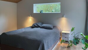 A bedroom with a bed, two bedside lamps, a window with a view of trees, and a potted plant. - 3 bedroom gorgeous home in Sæby (Sæby)