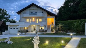 Uma casa moderna de dois andares com gramado bem cuidado, uma estátua na frente e iluminação externa.