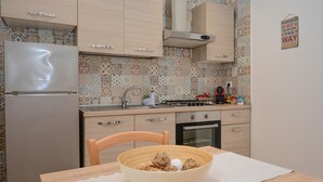 Cozinha com armários de madeira clara, geladeira de aço inoxidável, painel decorativo atrás do fogão e uma tigela sobre a mesa.