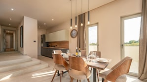 Un área de comedor moderna con una mesa dispuesta para cuatro, una cocina al fondo y una escalera que sube a un nivel superior.