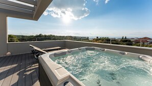 Terraza en la azotea con jacuzzi, cubierta de madera y vistas al mar y a la vegetación.
