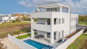 Una casa moderna de dos pisos con terraza en la azotea, piscina y jardín cuidado.