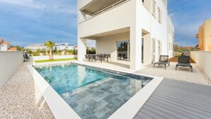 Una casa moderna de dos pisos con piscina, mobiliario exterior y vista del vecindario.