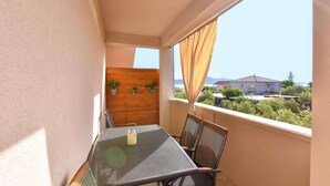 Ein Balkon mit Tisch und Stühlen, eine Holzwand mit Topfpflanzen und Blick auf Häuser und Grünflächen.