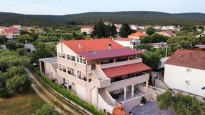 Ein mehrstöckiges Gebäude mit rotem Ziegeldach, einer überdachten Terrasse und Blick auf umliegende Häuser und Grünflächen.