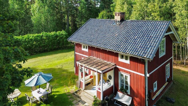 Une maison rouge à deux étages, dotée d’un porche abrité, d’une petite terrasse et d’une pelouse.