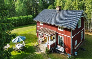 Een rode, twee verdiepingen tellende woning met een overdekte veranda, een klein terras en een gazon.