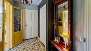 Un couloir avec des carreaux de sol à motifs, un meuble en bois doté d’un miroir et une porte jaune.