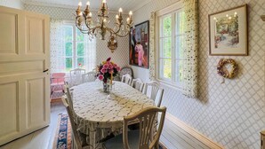 Une salle à manger avec une table ronde, des chaises, un lustre et une grande fenêtre avec des rideaux.