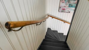 Une main courante en bois sur un mur blanc, avec un escalier noir.