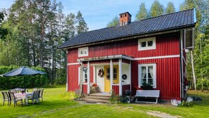 Une maison en bois rouge avec un porche, un petit jardin et une table entourée de chaises.