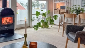 Uma sala de estar acolhedora com lareira a lenha, espaço de jantar com cadeiras, mesa com velas e plantas verdes grandes.