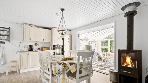 A cozy kitchen with white cabinets, a dining table with chairs, a hanging light fixture, and a wood-burning stove. - Amazing home in Tarm with WiFi (Tarm)