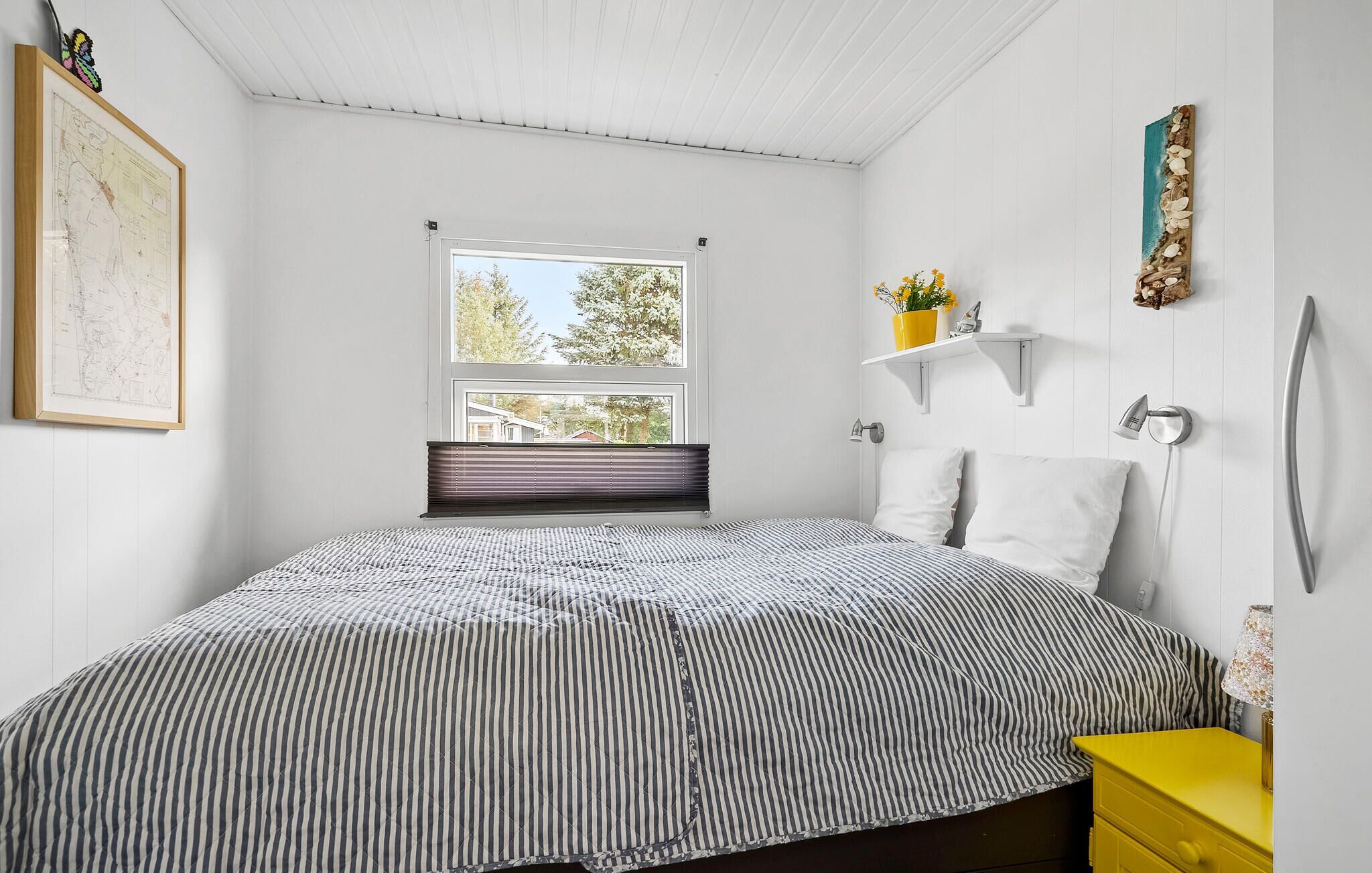 Une chambre à coucher avec un lit, une fenêtre, une carte accrochée au mur et une étagère ornée de fleurs.