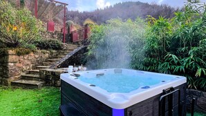 A hot tub with a stone staircase leading up to a red structure, surrounded by lush greenery. - Pet friendly home in Genestelle (Genestelle)