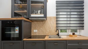 Une cuisine moderne avec des meubles de couleur sombre, un four encastré et une fenêtre équipée de stores horizontaux.