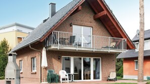 Een tweelaags huis met een bakstenen gevel, een balkon met een metalen hekwerk en een schuifdeur die leidt naar een overdekt patio.