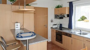 Een functionele keuken met houten kastjes, een inbouwoven, een spoelbak en een klein eethoekje met een stoel.