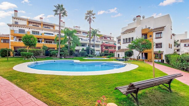 A pool surrounded by well-maintained grass, palm trees, and a bench. - Amazing apartment in Costa Esuri - Ayamonte (Costa Esuri - Ayamonte)