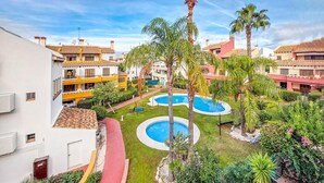 A hotel courtyard with multiple swimming pools, palm trees, and a red pathway. - Amazing apartment in Costa Esuri - Ayamonte (Costa Esuri - Ayamonte)