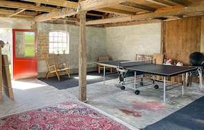 A room with a ping pong table, chairs, a red door, and a window.