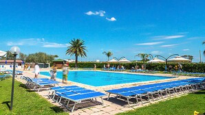 A swimming pool with blue lounge chairs and umbrellas, surrounded by greenery and palm trees. - Cozy home in Tarquinia with swimming pool (Tarquinia)