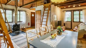 Interior rústico de una cabaña con comedor, muebles de madera, chimenea y un espacio en el altillo.