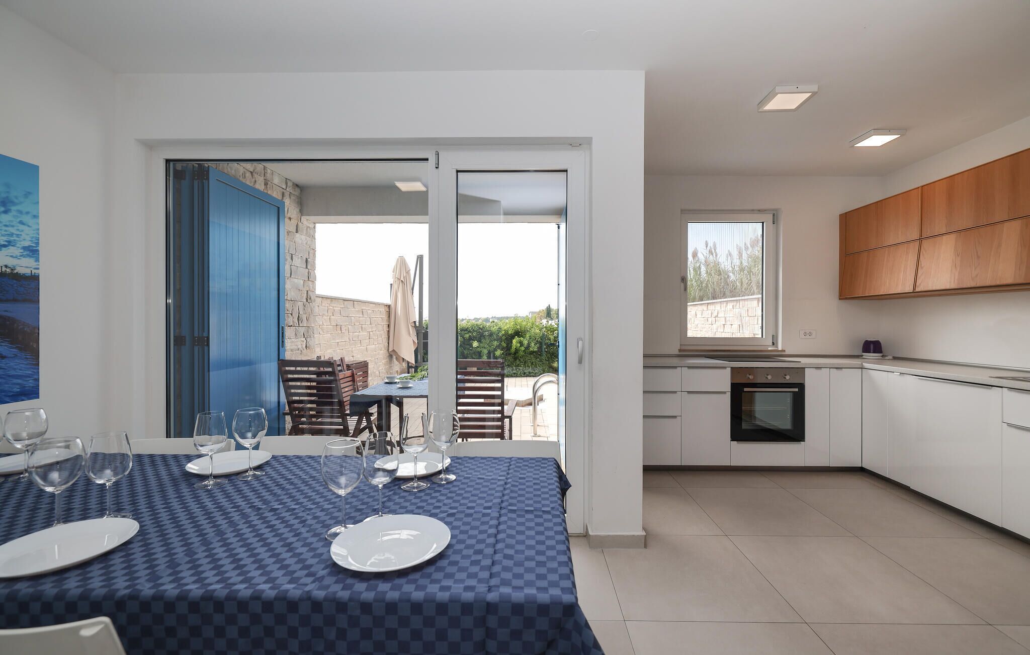 Una cuina moderna amb armaris blancs, forn integrat i finestra amb vista a un jardí.
