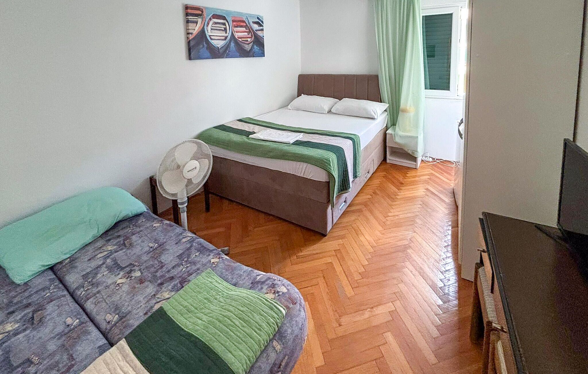 A bedroom with two beds, a standing fan, and a painting on the wall.