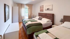 Une chambre d’hôtel avec deux lits, un bureau, une chaise, une fenêtre avec des rideaux, un ventilateur fixé au mur et des œuvres d’art accrochées au mur.