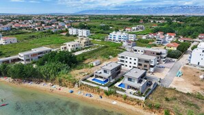 Ein Küstenwohngebiet mit modernen Gebäuden, einem Strand mit Liegestühlen und einer bergigen Kulisse.