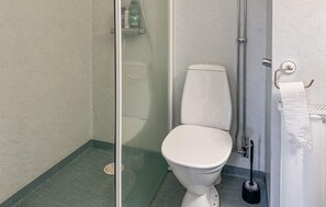 A bathroom with a toilet, a glass shower enclosure, and a toilet brush.