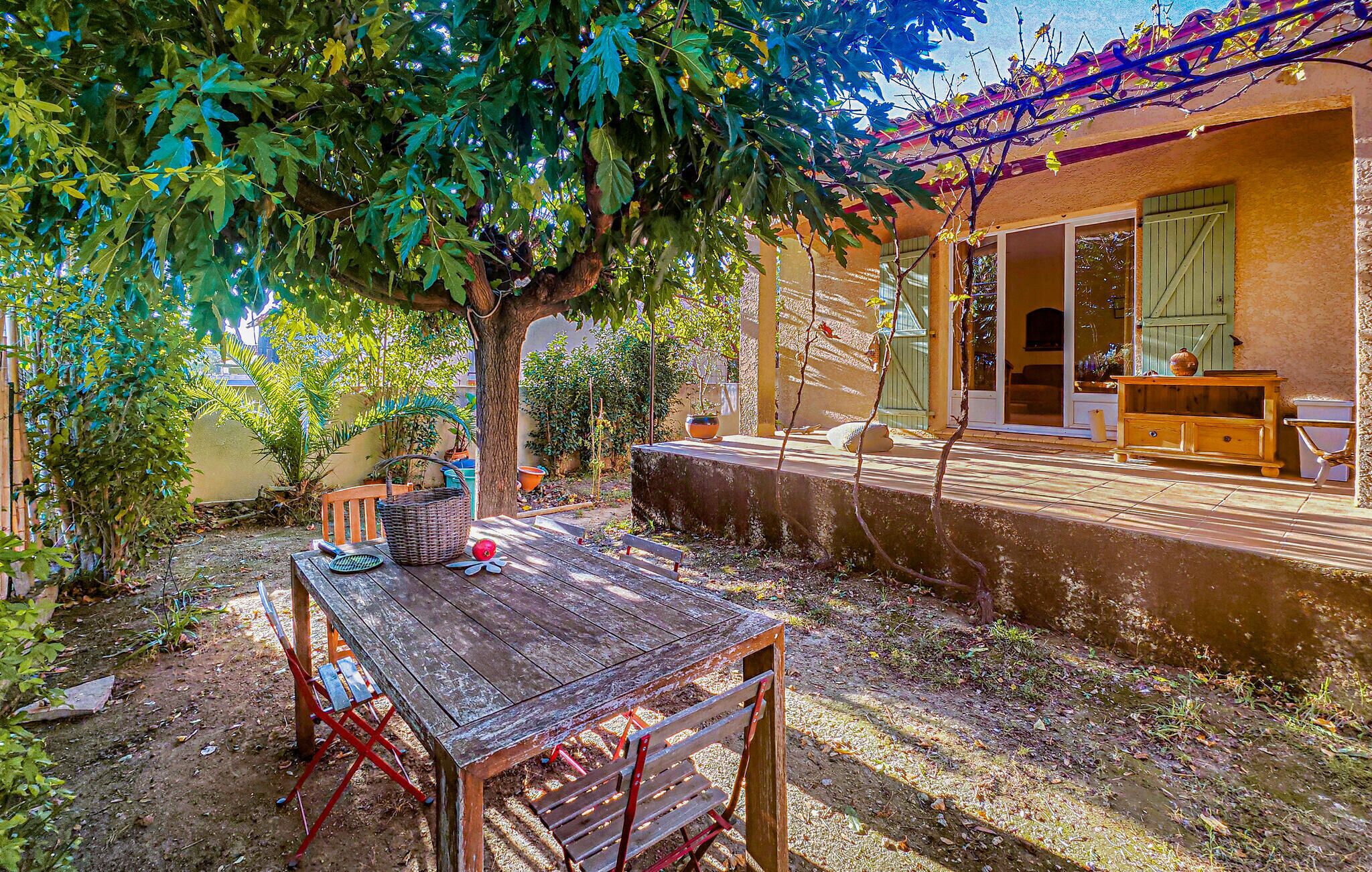 A rustic outdoor patio with a wooden table and chairs, surrounded by greenery and a pergola.