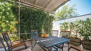 Un patio al aire libre con una mesa y sillas, rodeado de vegetación y un edificio blanco al fondo.