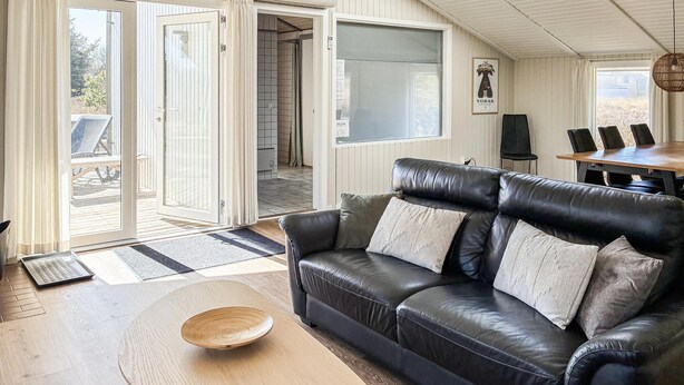 En moderne stue med en lædersofa, et træsofabord og et spiseområde med bord og stole.