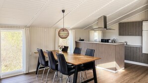 Et moderne køkken med en central ø, et træspisebord med stole, og et stort vindue med gardiner.