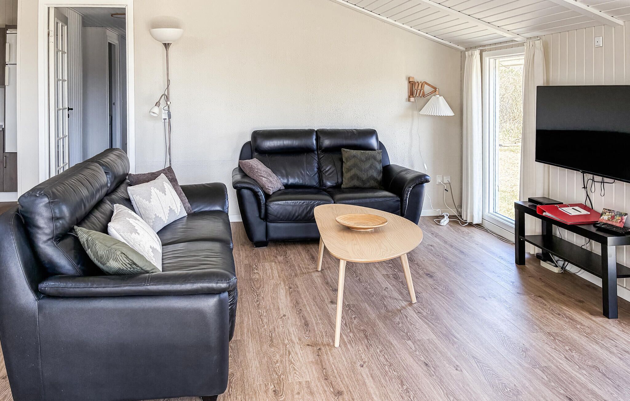 A living room with two black leather sofas, a wooden coffee table, a TV on a stand, and a floor lamp.