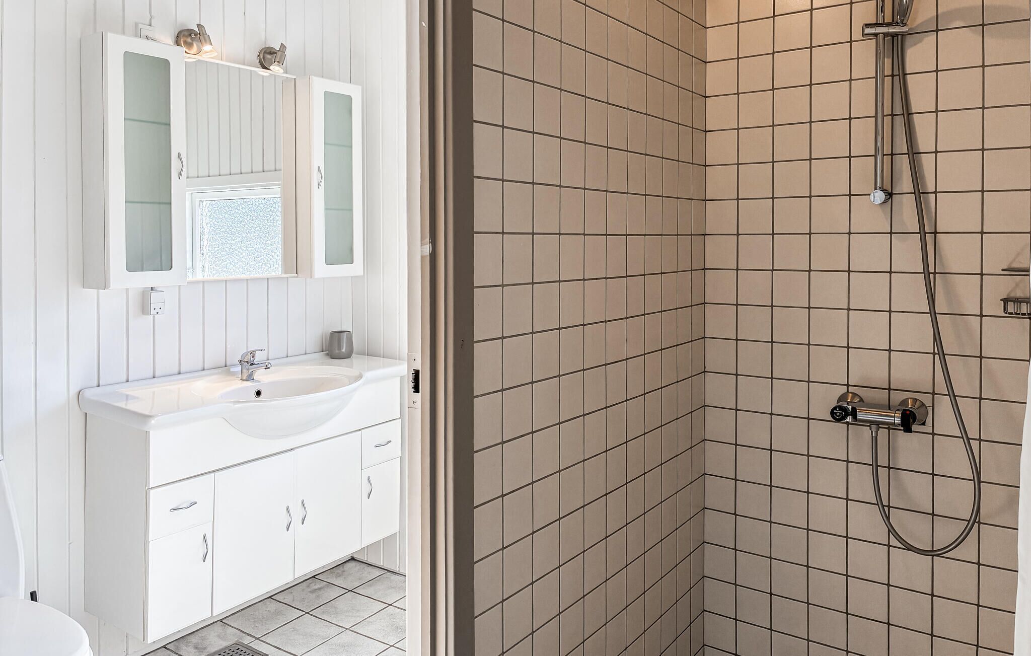 Un baño con tocador blanco, lavabo y ducha con azulejos color beige.