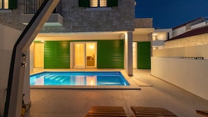 Un espace piscine extérieur moderne, agrémenté d’un mur en pierre, de volets verts et d’une terrasse en bois.