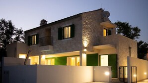 Une maison à deux étages avec une façade en pierre, des volets verts et une antenne parabolique.